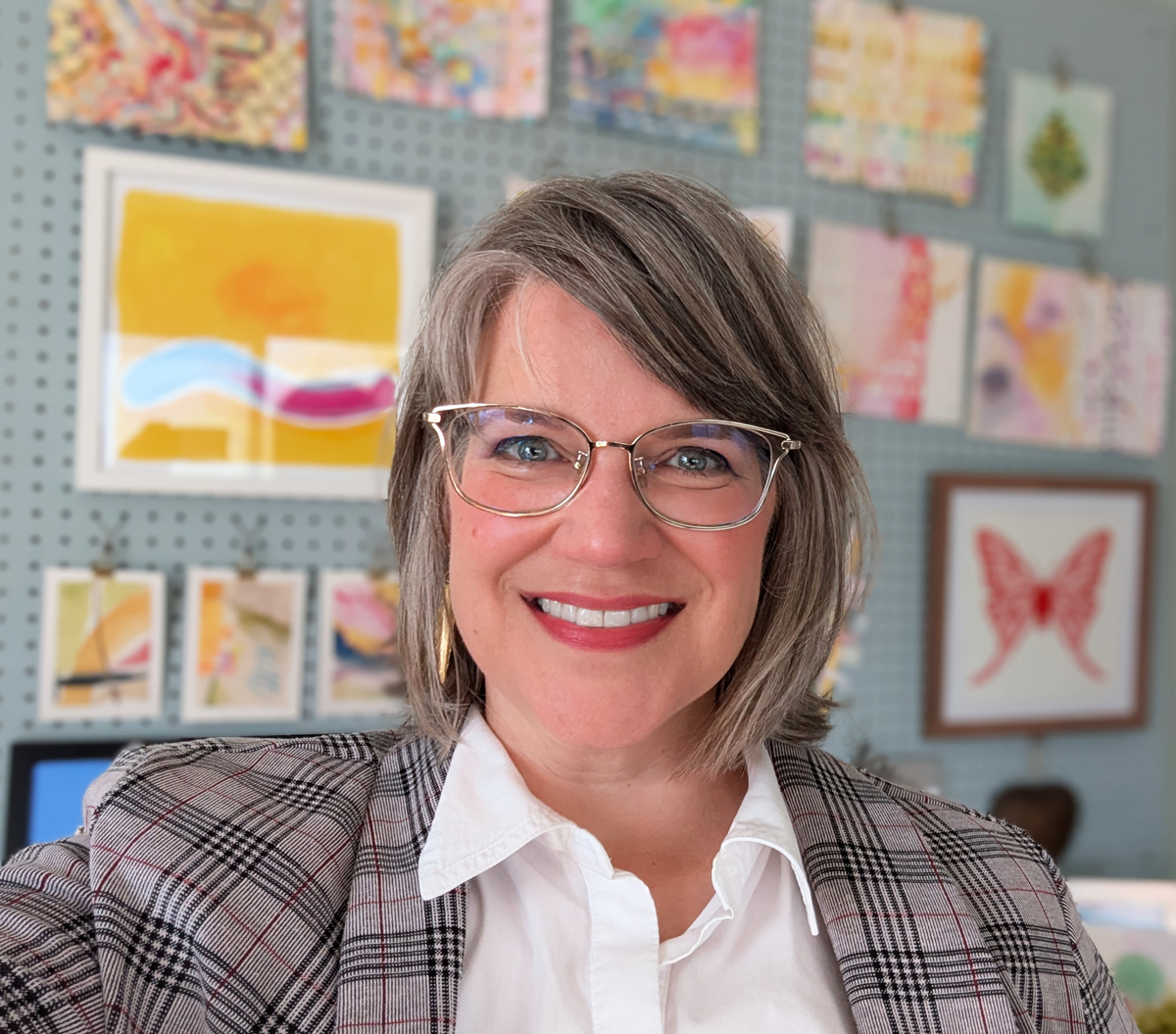 A woman smiles in front of colorful artwork.