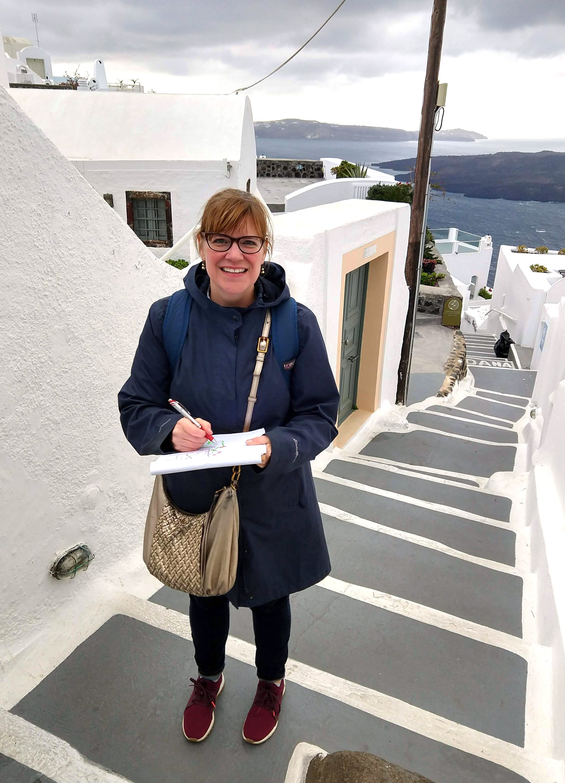 A woman stands outdoors on steps with a clipboard